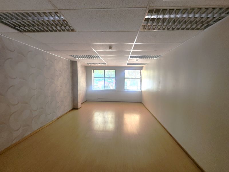 An empty, open-plan office space featuring a suspended ceiling with recessed lighting, laminate flooring, and a feature wallpaper wall.