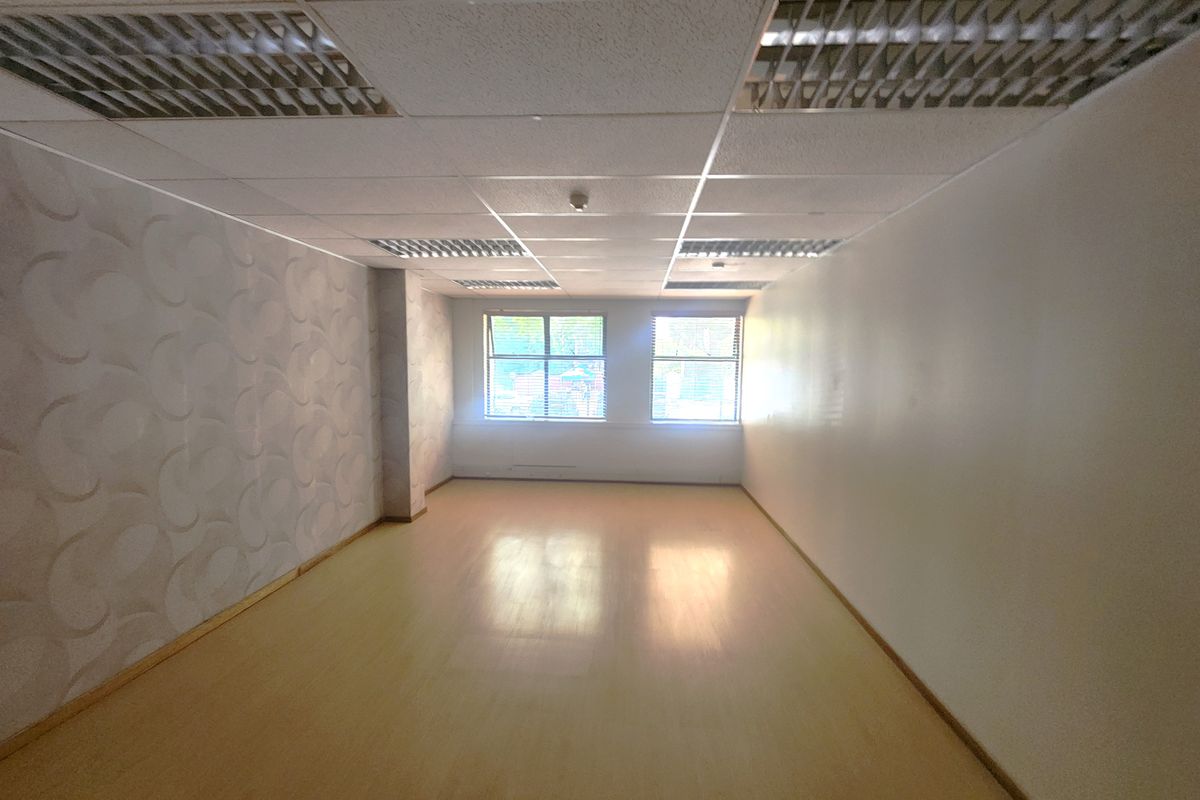 An empty, open-plan office space featuring a suspended ceiling with recessed lighting, laminate flooring, and a feature wallpaper wall.