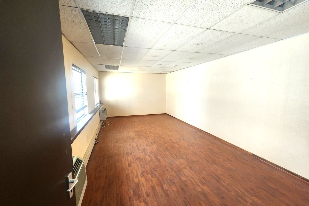 An empty office space featuring laminate flooring, a suspended ceiling with recessed lighting, and a built-in window air conditioning unit.