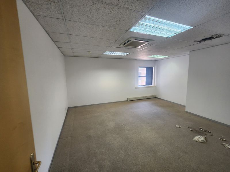 An empty office space featuring a suspended ceiling, recessed lighting, and carpeted flooring, currently requiring minor repairs to the ceiling and floor.