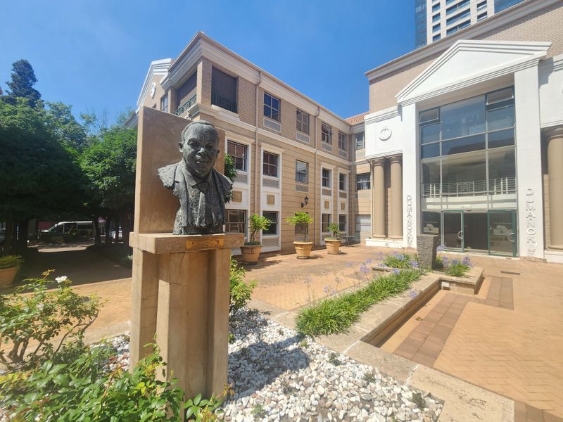 A well-maintained office building exterior featuring a paved courtyard, brick facade, and a prominent entrance with architectural columns.