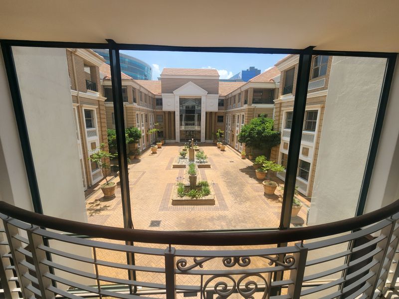 A view from an interior balcony overlooking a well-maintained paved office courtyard with central landscaping and brick building facades.