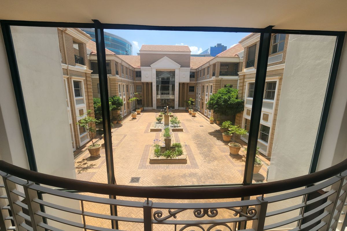 A view from an interior balcony overlooking a well-maintained paved office courtyard with central landscaping and brick building facades.