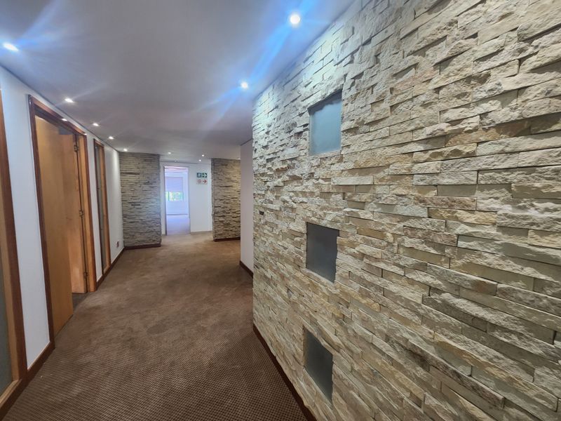A well-maintained office hallway featuring a decorative stone-clad feature wall with integrated glass inserts, recessed ceiling lighting, and carpeted flooring.