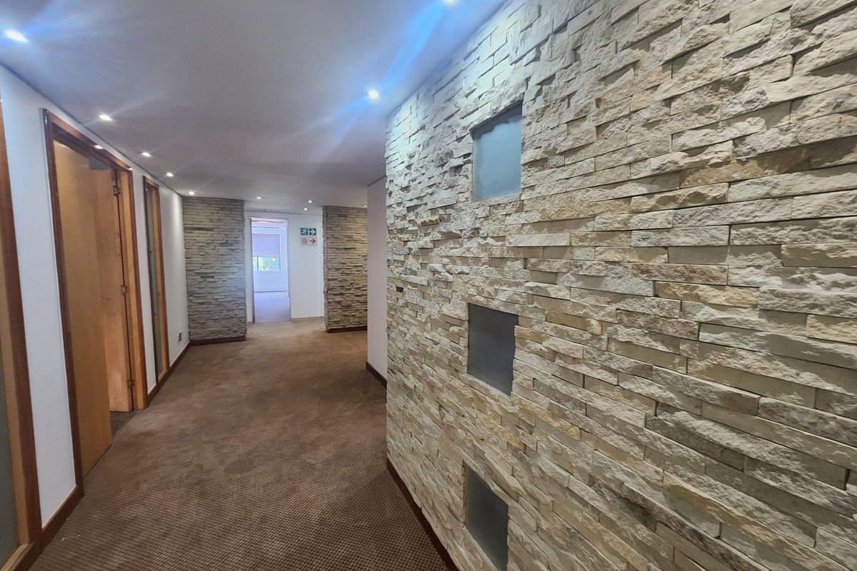 A well-maintained office hallway featuring a decorative stone-clad feature wall with integrated glass inserts, recessed ceiling lighting, and carpeted flooring.