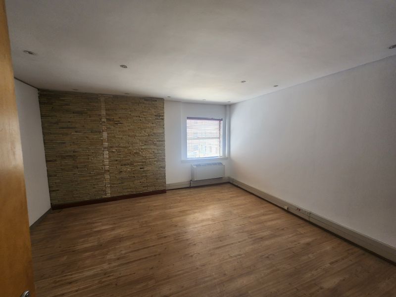 A bright, empty office space featuring a stone accent wall, laminate flooring, recessed lighting, and a built-in HVAC unit.