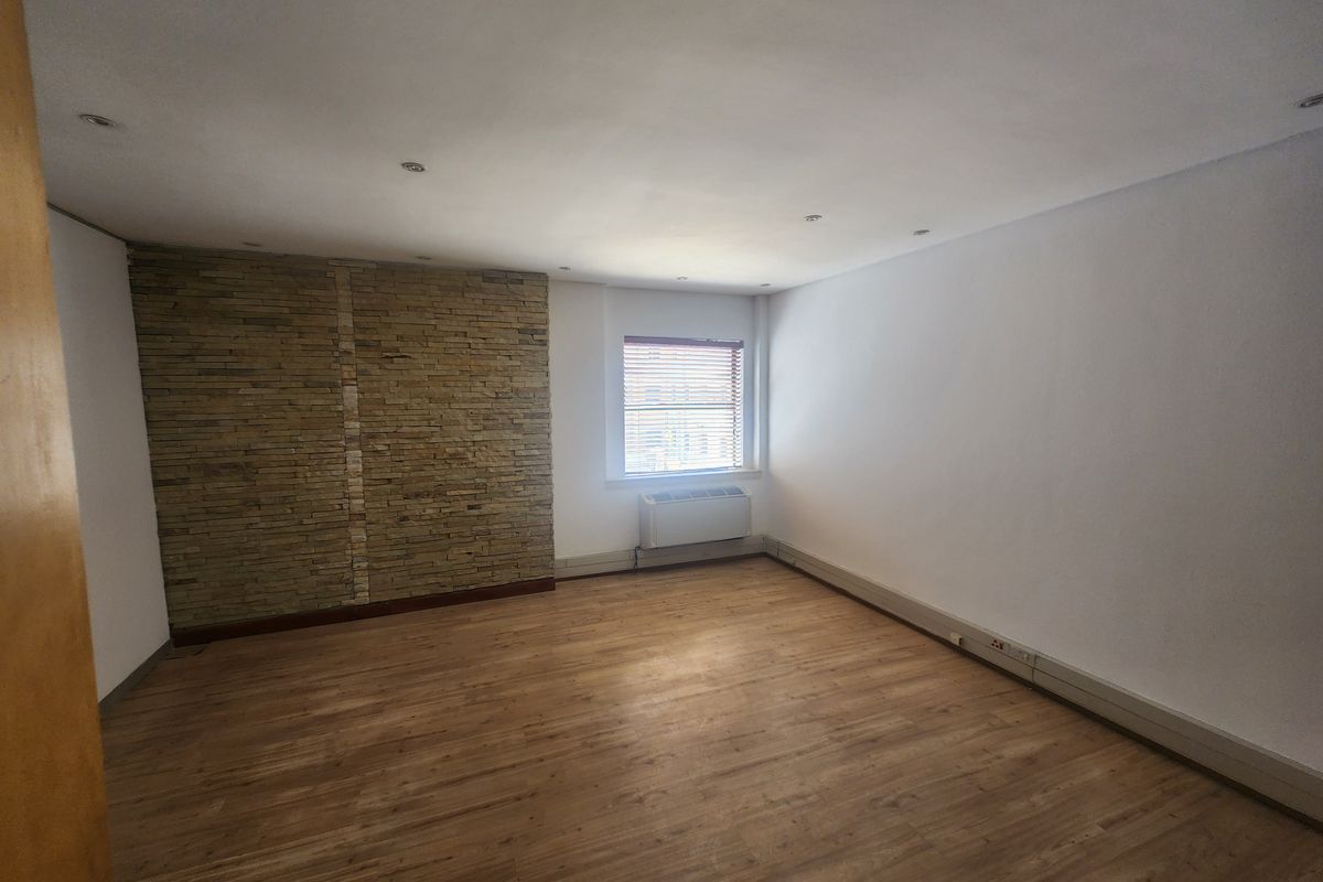 A bright, empty office space featuring a stone accent wall, laminate flooring, recessed lighting, and a built-in HVAC unit.