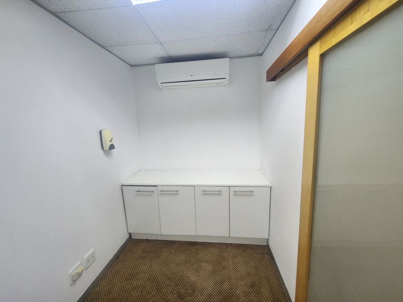 A small office space featuring built-in white cabinetry, a wall-mounted air conditioning unit, and a sliding door entrance.