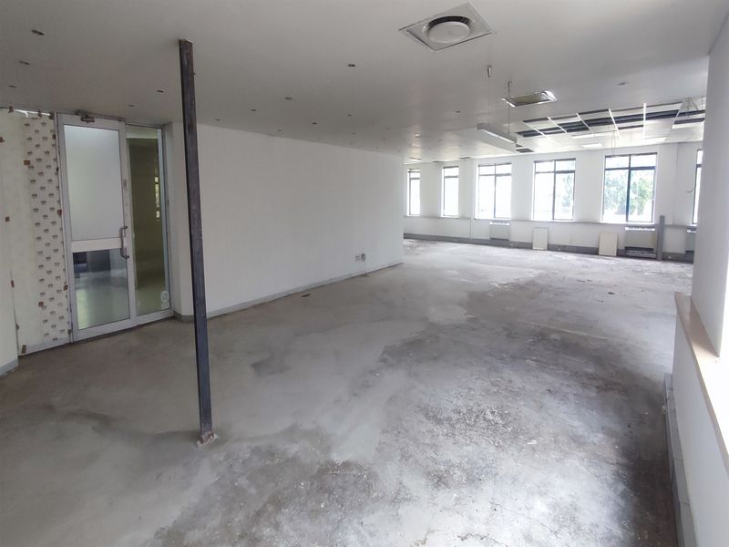 An open-plan office space in shell condition, featuring large windows, recessed lighting, and unfinished concrete flooring, ready for custom fit-out.