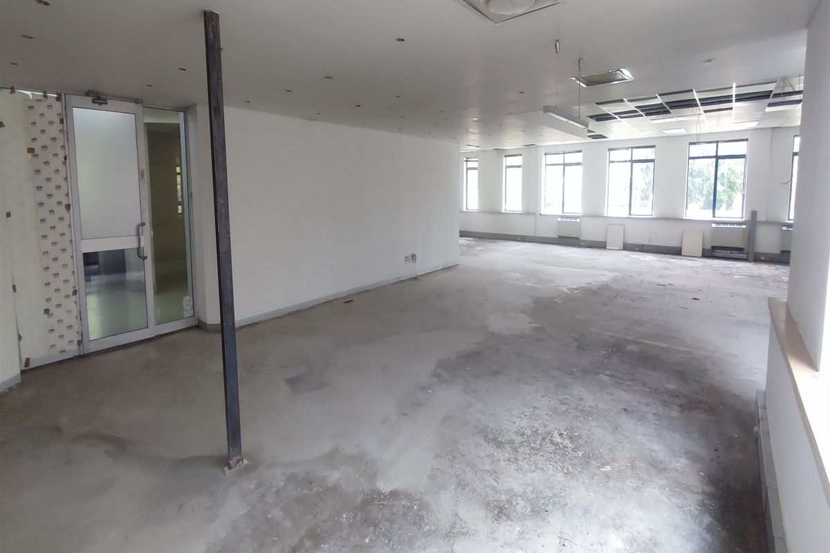 An open-plan office space in shell condition, featuring large windows, recessed lighting, and unfinished concrete flooring, ready for custom fit-out.