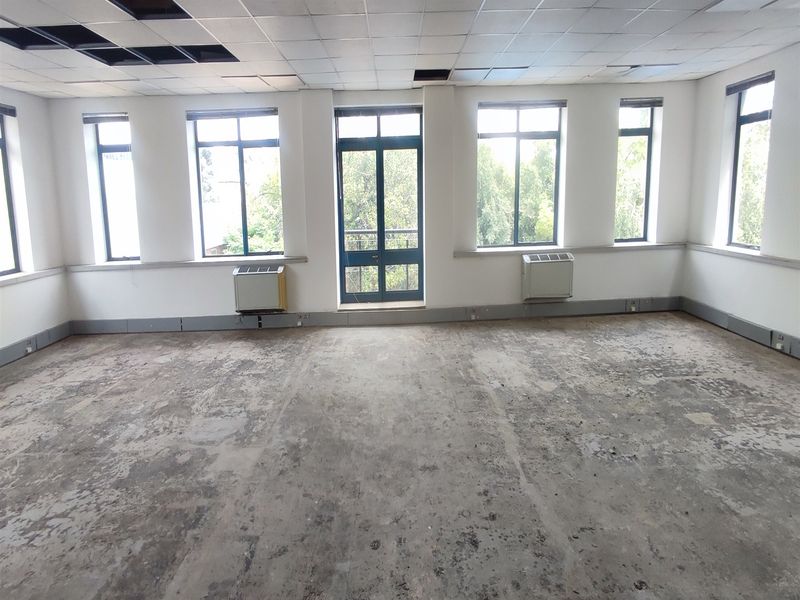 Spacious, vacant office suite featuring large windows, air conditioning units, and a suspended ceiling requiring maintenance and flooring refurbishment.