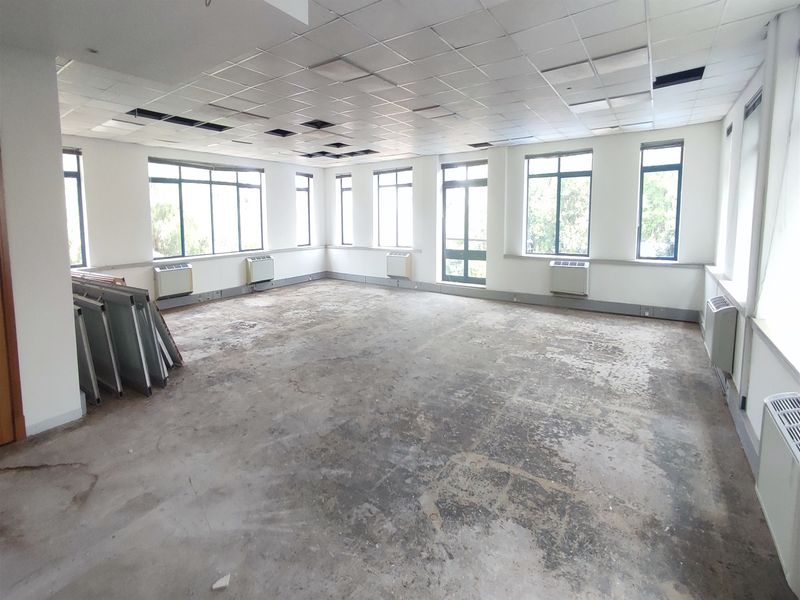 Spacious open-plan office area featuring large windows, air conditioning units, and a suspended ceiling, currently in need of flooring and ceiling repairs.
