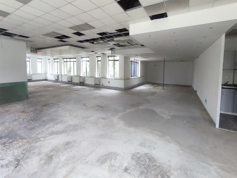 Spacious open-plan office area featuring large windows, a small kitchenette, and a suspended ceiling requiring repair and refurbishment.