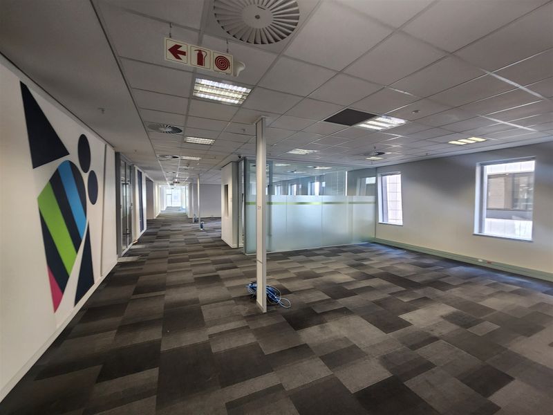 Spacious open-plan office area featuring suspended ceilings, recessed lighting, carpet tiles, and glass partitioning, providing a clean and professional workspace environment.