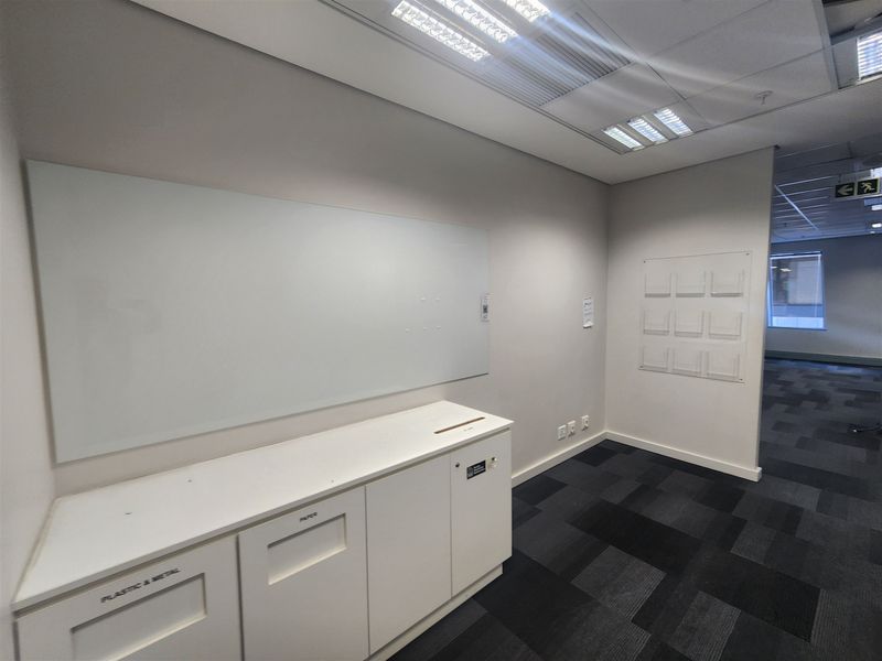 A clean, professional office space featuring built-in cabinetry, a glass whiteboard, wall-mounted brochure holders, and modern carpet tiles.