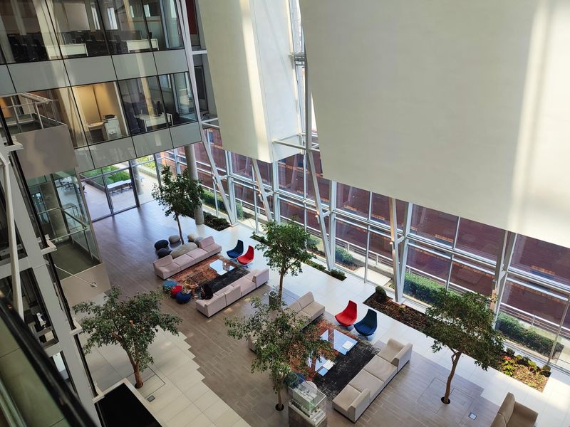Spacious modern office atrium featuring high ceilings, extensive glass curtain walls, and an open-plan lounge area with integrated indoor landscaping.