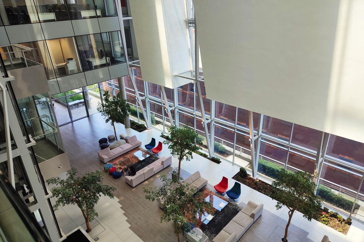 Spacious modern office atrium featuring high ceilings, extensive glass curtain walls, and an open-plan lounge area with integrated indoor landscaping.