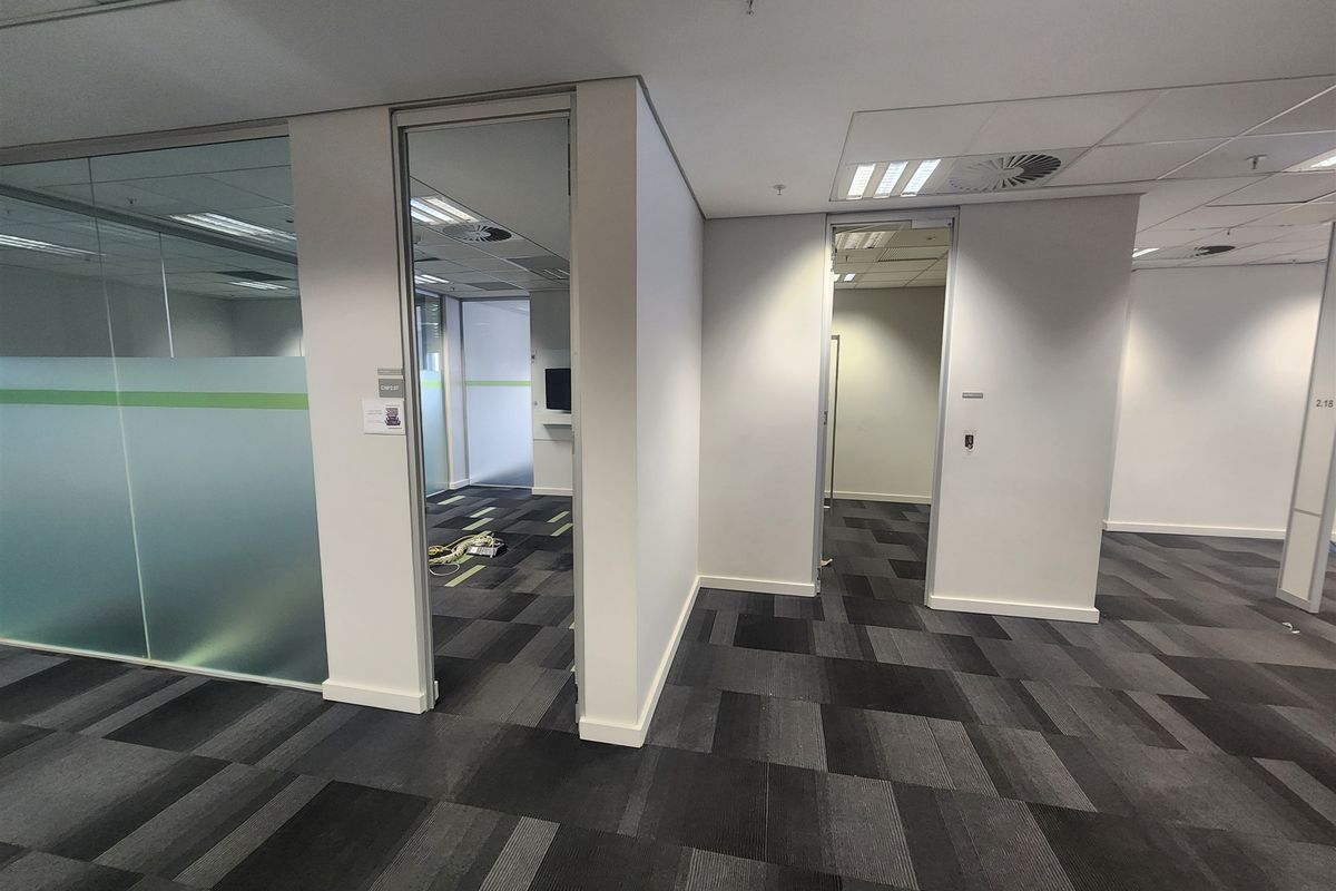 Modern vacant office space featuring glass partitions, suspended ceilings with recessed lighting, and durable carpet tiles throughout the open-plan layout.