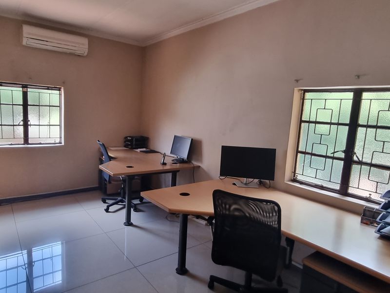 A functional office space featuring tiled flooring, split-system air conditioning, and windows fitted with security bars.
