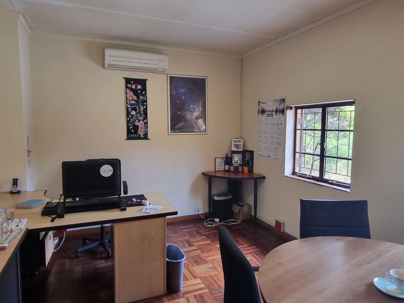 A functional office space featuring parquet flooring, a wall-mounted air conditioning unit, and windows fitted with security bars.