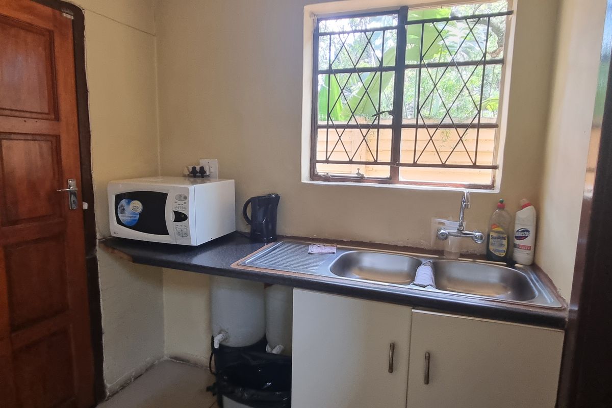 A compact kitchen area featuring a double sink, built-in cabinetry, and a window with security bars, offering a functional space for office utility needs.