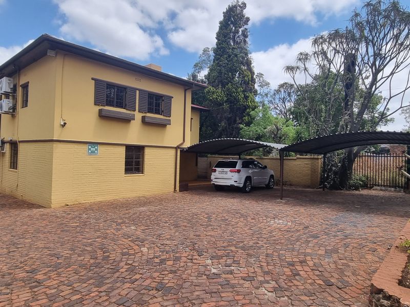 Exterior view of the office property featuring a paved driveway, covered carport parking, and yellow brick facade with mounted air conditioning units.
