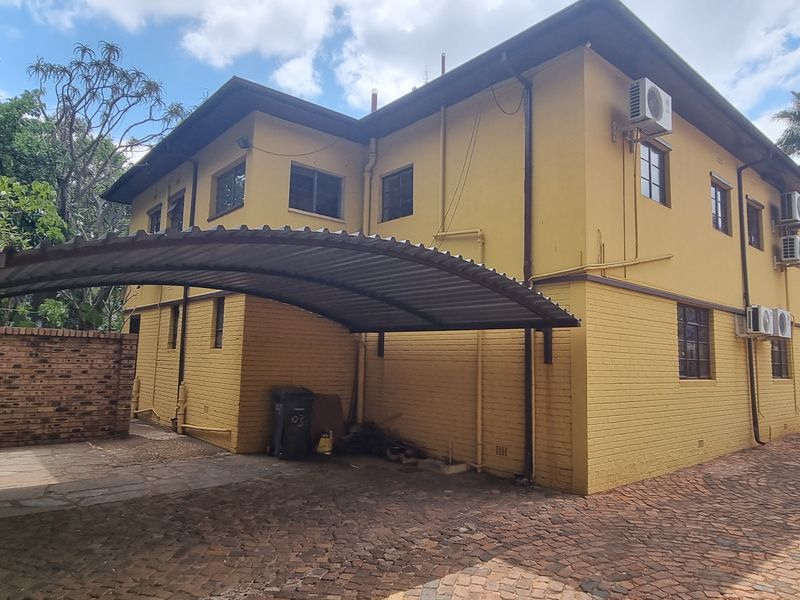 Rear exterior view of the office building featuring a covered carport, brick paved driveway, and multiple wall-mounted air conditioning units.