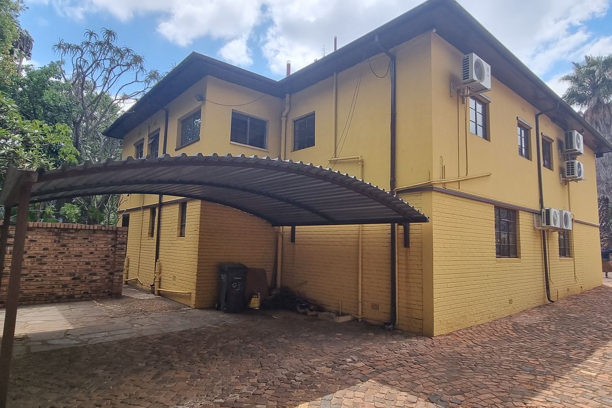 Rear exterior view of the office building featuring a covered carport, brick paved driveway, and multiple wall-mounted air conditioning units.