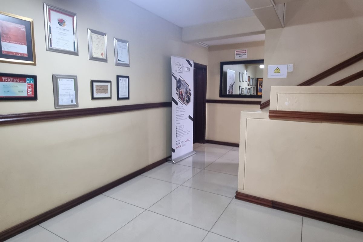 A clean, well-maintained office hallway featuring tiled flooring, a wooden dado rail, and a staircase balustrade.
