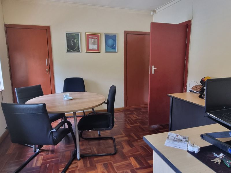 A functional office space featuring warm parquet flooring, natural light from a side window, and two solid core access doors.