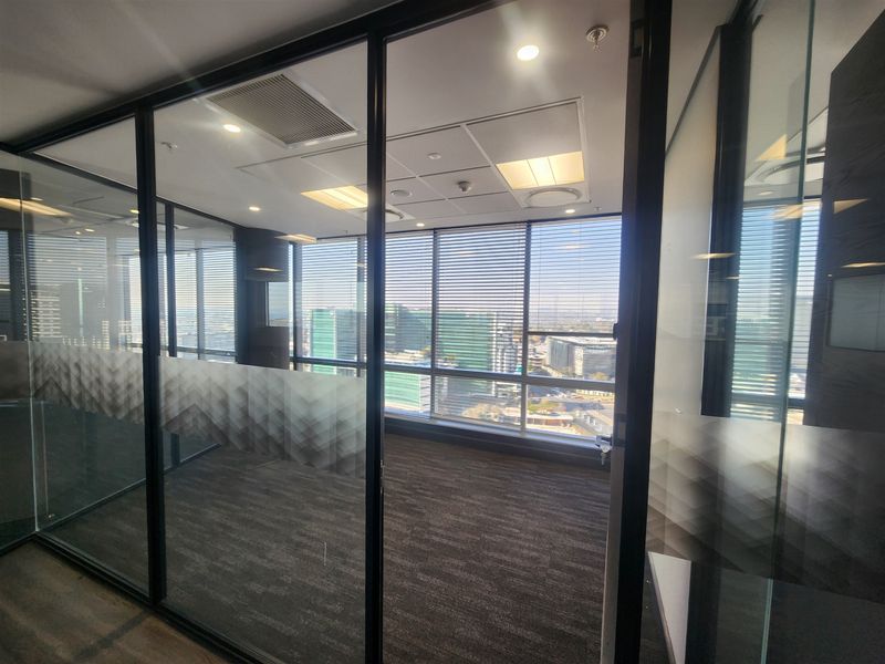 A modern, empty office space featuring glass partitions, carpeted flooring, and large windows with venetian blinds, offering a professional environment with natural light.
