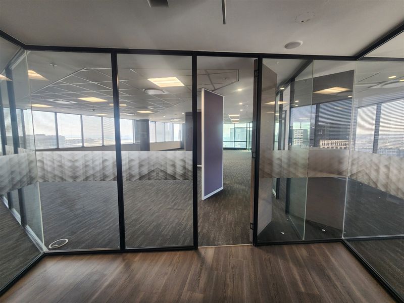 A modern, vacant office space featuring glass partitions, suspended ceilings, and a combination of carpet and laminate flooring with expansive city views.