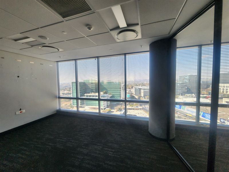 A bright, empty office space featuring floor-to-ceiling windows with city views, a suspended ceiling, and modern glass partitioning.