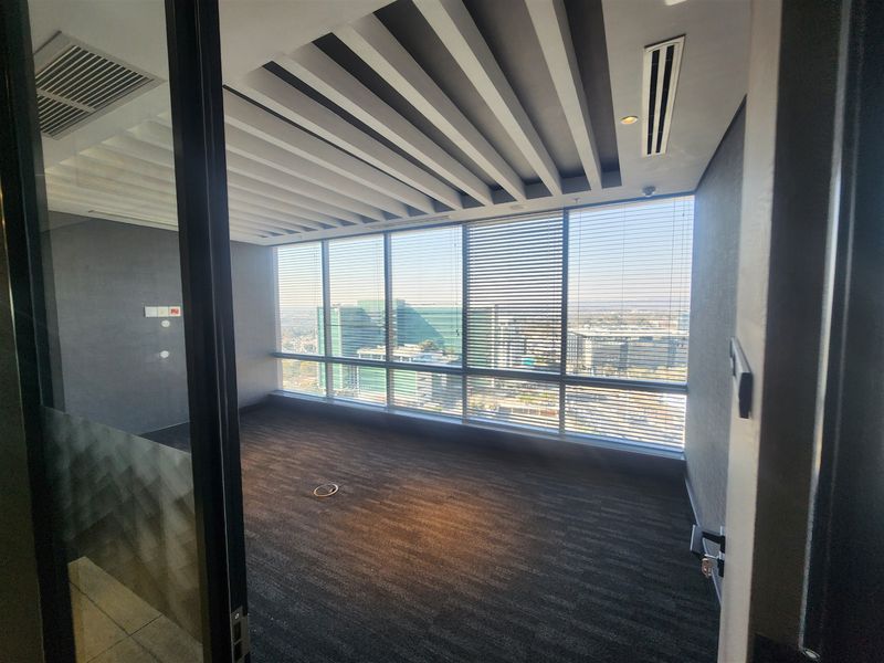 A modern, empty office space featuring floor-to-ceiling windows with city views, a unique slatted ceiling design, and integrated ducted air conditioning.