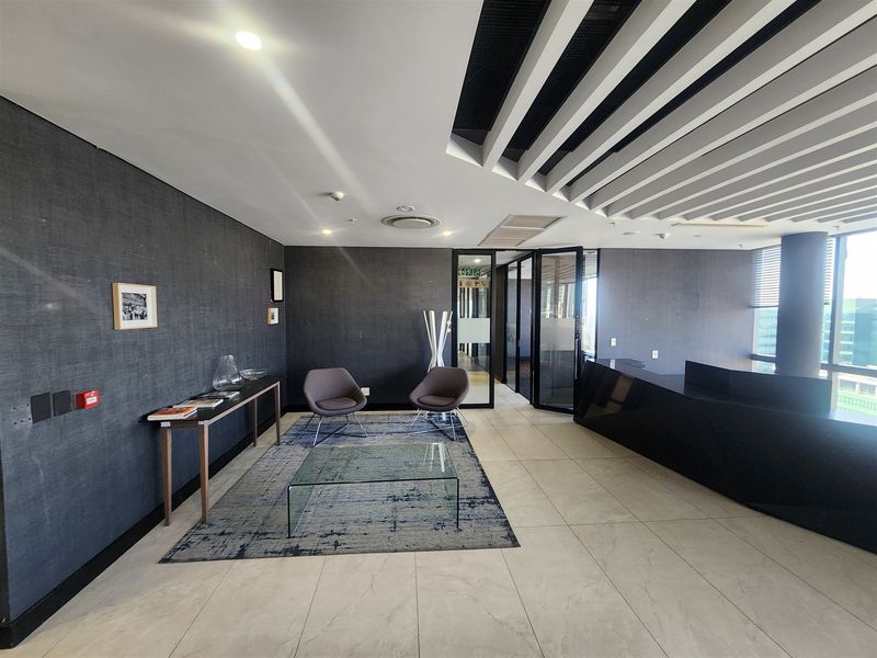 Modern office reception area featuring a sleek built-in desk, contemporary slatted ceiling design, and large glass partitions providing a professional workspace environment.