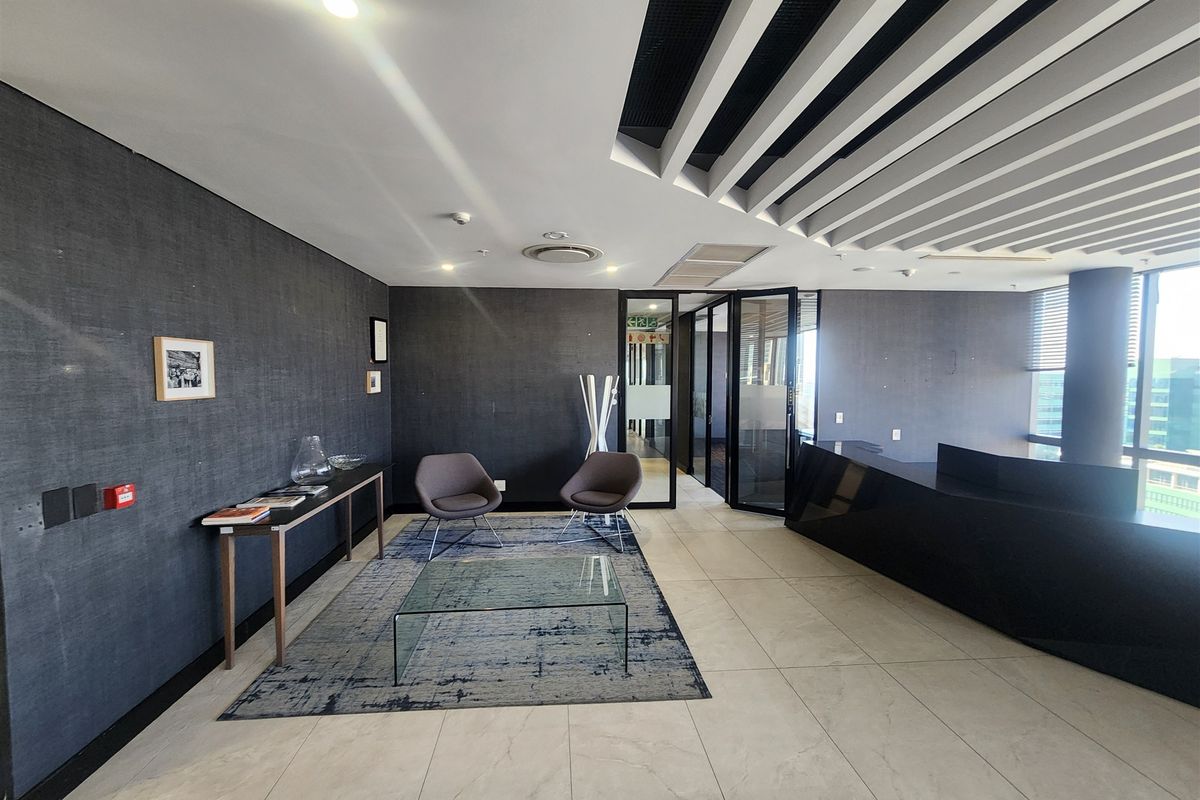 Modern office reception area featuring a sleek built-in desk, contemporary slatted ceiling design, and large glass partitions providing a professional workspace environment.