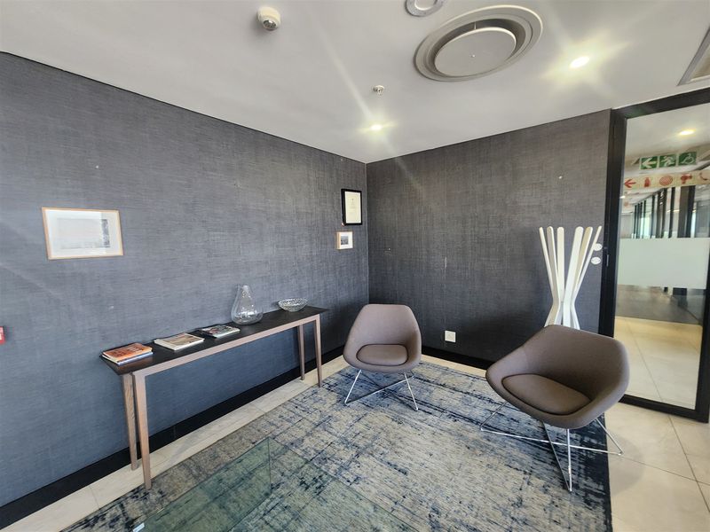 A professional office waiting area featuring dark textured wallpaper, recessed ceiling lighting, and a modern glass partition entrance.