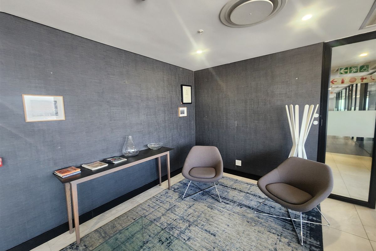 A professional office waiting area featuring dark textured wallpaper, recessed ceiling lighting, and a modern glass partition entrance.