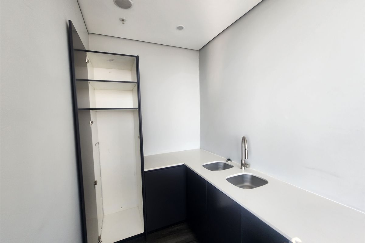 A clean, modern office kitchenette featuring dark built-in cabinetry, stone countertops, and a double stainless steel sink with a contemporary mixer tap.