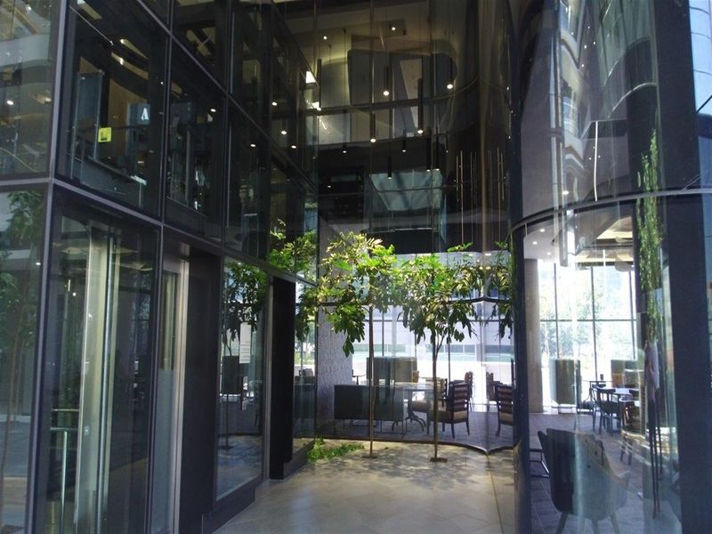 Modern office building entrance lobby featuring extensive glass curtain walling, high ceilings with recessed lighting, and premium stone flooring.