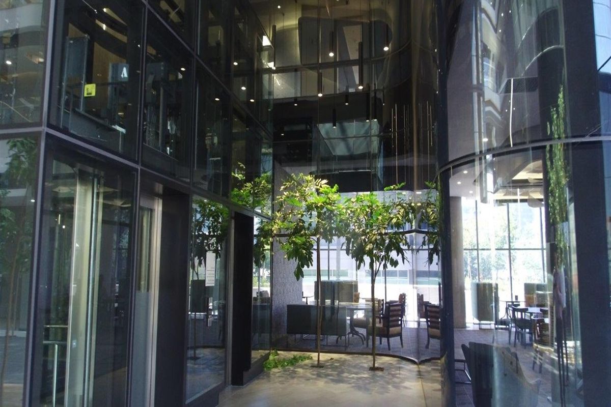 Modern office building entrance lobby featuring extensive glass curtain walling, high ceilings with recessed lighting, and premium stone flooring.
