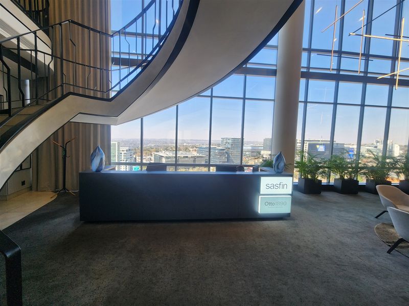 Modern office reception area featuring a striking curved staircase, floor-to-ceiling glass facade with panoramic city views, and a professional built-in reception desk.