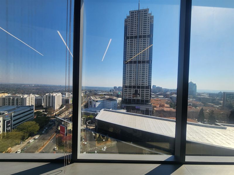 An elevated urban view from a high-rise office space featuring large floor-to-ceiling windows overlooking the surrounding city skyline.
