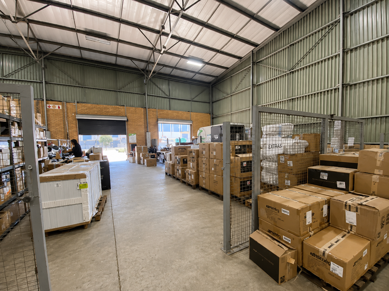 Spacious industrial warehouse unit featuring high ceilings with exposed steel trusses, concrete flooring, and secure metal mesh partitioning for organized storage.