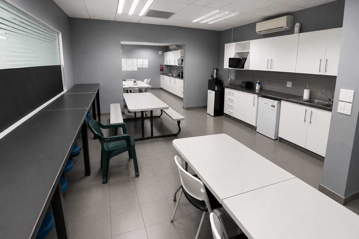 A functional industrial kitchen and breakroom area featuring white cabinetry, stainless steel sink, tiled flooring, and integrated air conditioning.