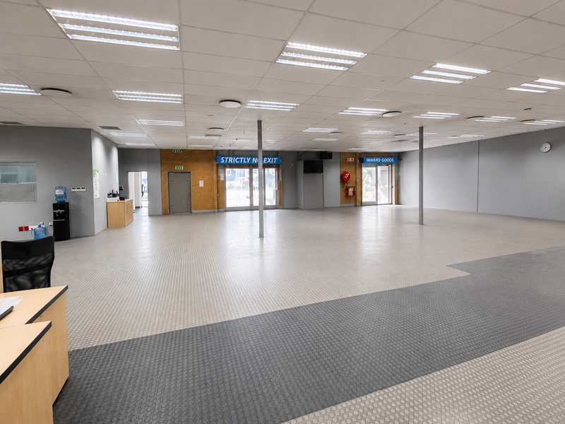 Spacious open-plan industrial warehouse or office area featuring durable rubber flooring, suspended ceilings with integrated lighting, and multiple access points.