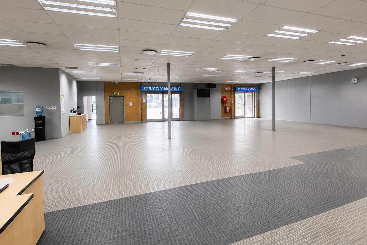 Spacious open-plan industrial warehouse or office area featuring durable rubber flooring, suspended ceilings with integrated lighting, and multiple access points.