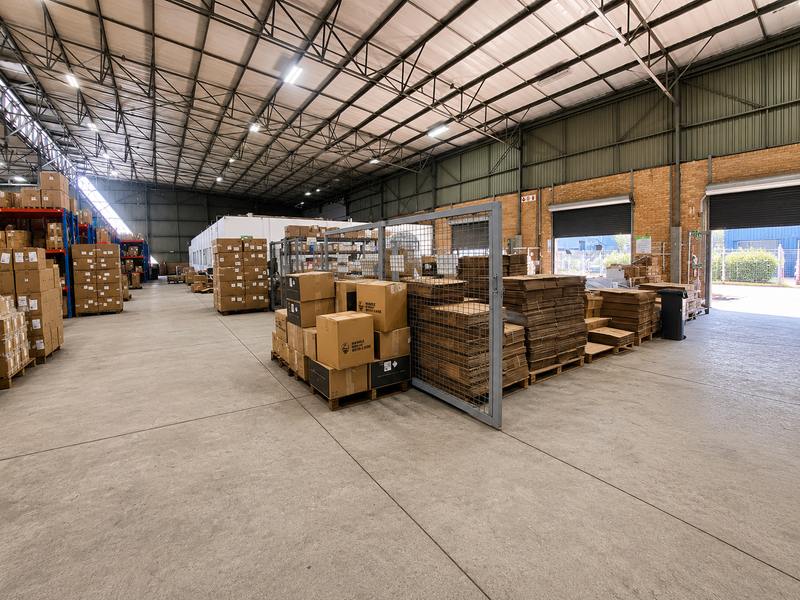 Spacious industrial warehouse featuring high-clearance steel truss roofing, polished concrete floors, and multiple roller shutter access points for efficient logistics and storage operations.