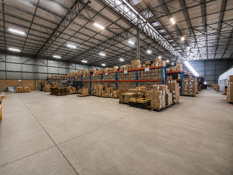 Spacious industrial warehouse featuring high-clearance steel truss roofing, polished concrete flooring, and extensive integrated pallet racking systems for efficient storage.