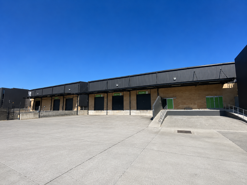 Industrial warehouse exterior featuring multiple loading docks with roller shutter doors and a spacious concrete yard area.